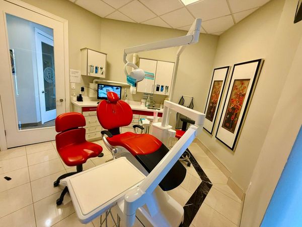 Dental operatory with red chair, white cabinets, and framed artwork.