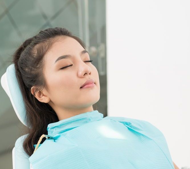 Woman in a dentist chair, eyes closed, wearing a blue bib, serene expression.