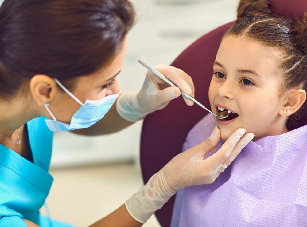 Dentist examining a young girl's teeth in a dental office. The girl smiles.