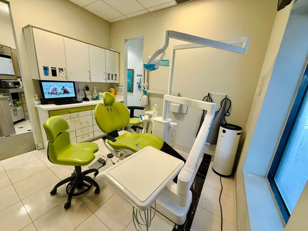 Dental operatory with green chair, equipment, cabinets, and window.