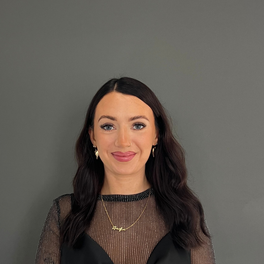 A woman wearing a white jacket and earrings is smiling for the camera.