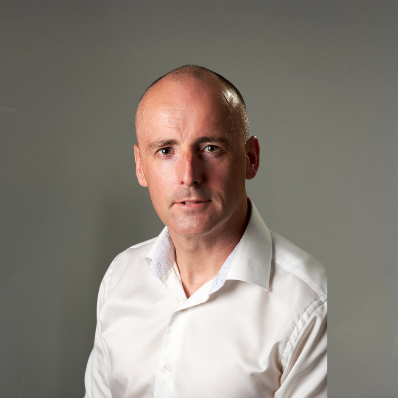 A bald man in a suit and blue shirt is smiling for the camera.