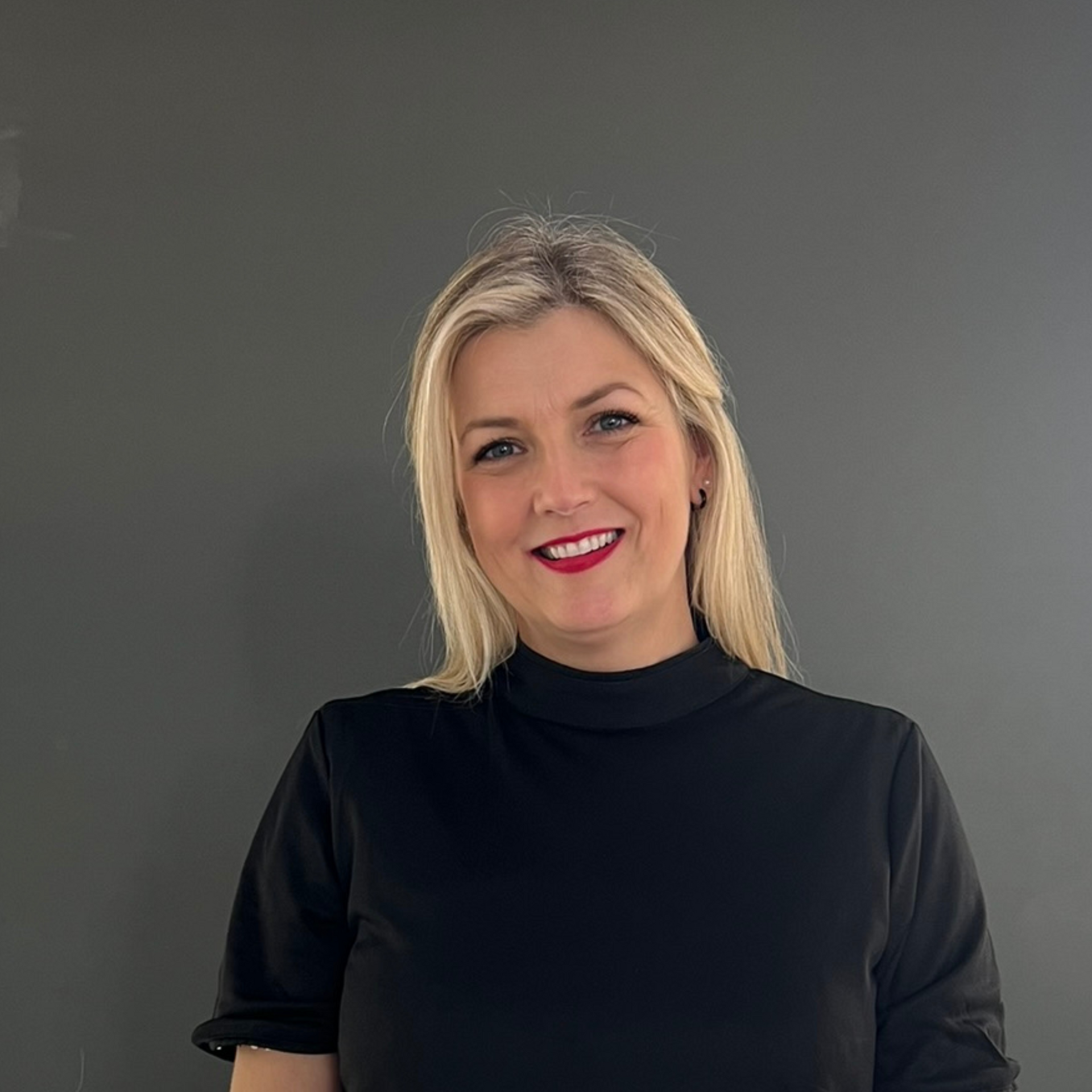 A woman with blonde hair is smiling for the camera while wearing a white jacket.