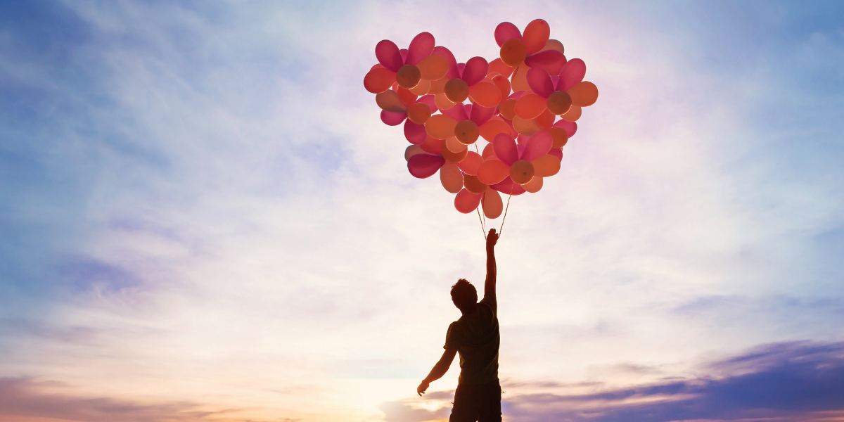 A man is holding a bunch of balloons in the shape of a heart.