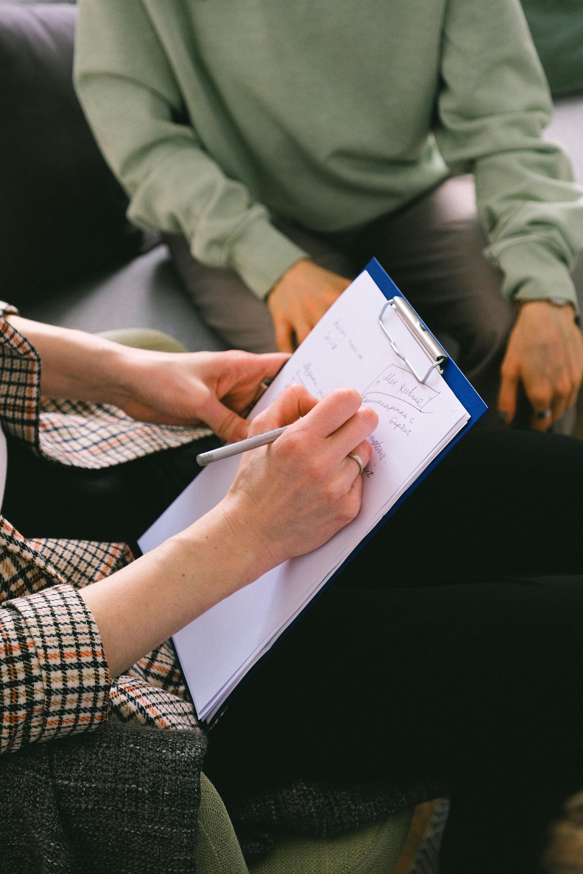 A woman is writing on a clipboard while sitting on a couch.