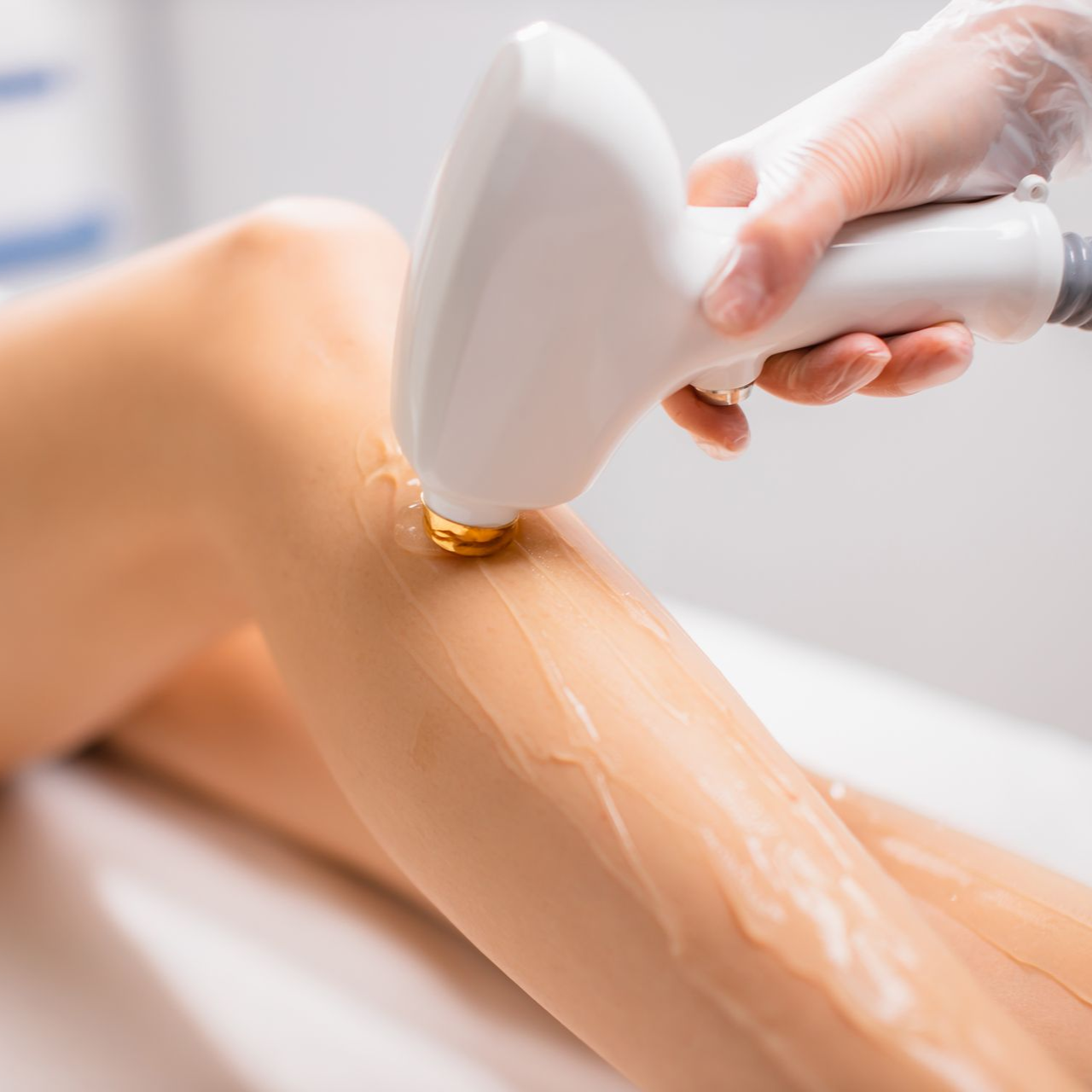 Eine Hand, die ein Wachsgerät hält, gleitet in einer Spa-Umgebung mit warmem Wachs über das Bein einer Person.