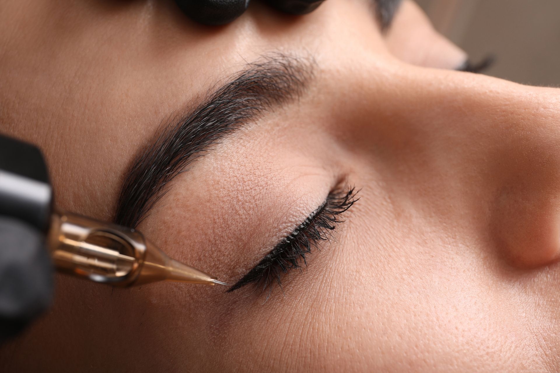 Nahaufnahme einer Person, die sich Permanent-Eyeliner mit einer Tätowiernadel in der Nähe des Augenlids machen lässt.