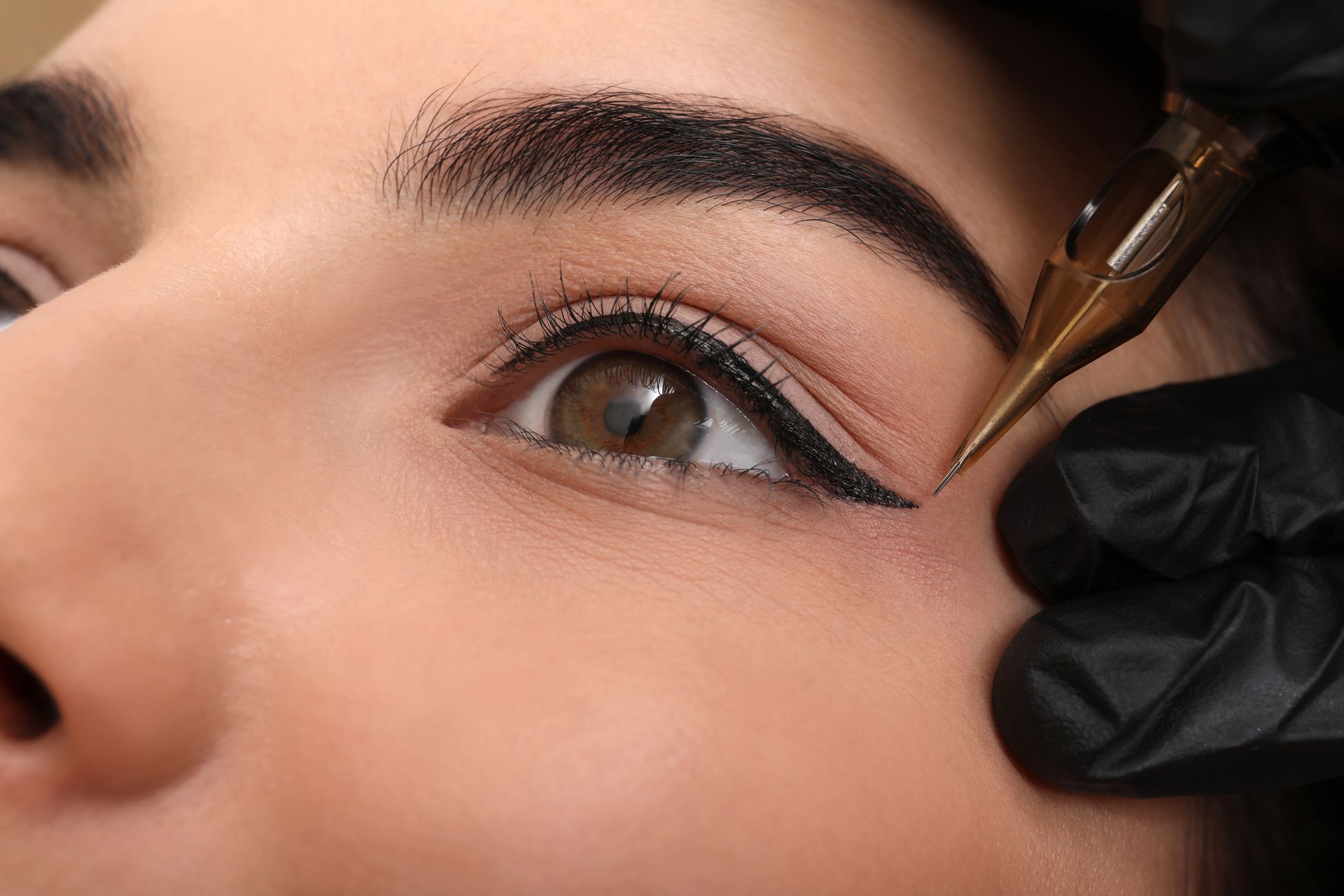 Nahaufnahme eines Auges, das mit schwarzem Eyeliner von einer behandschuhten Hand und einem Pinsel umrandet wird.