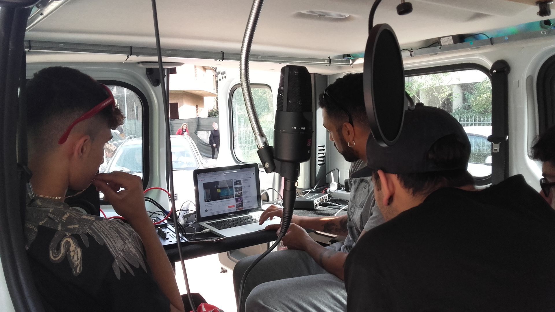 Persone che registrano musica in un furgone, con un microfono, un computer portatile e un'attrezzatura per la registrazione.