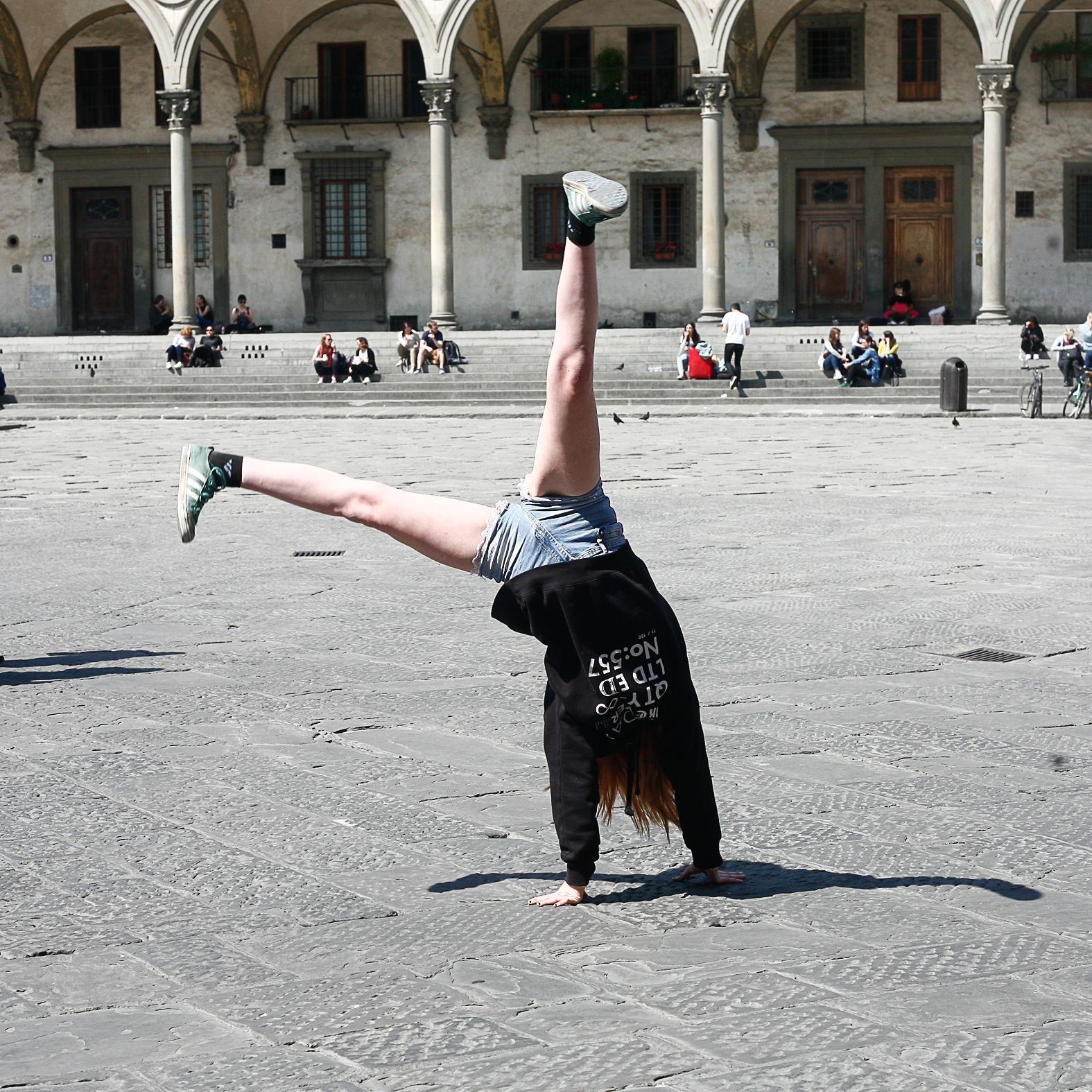 Persona che fa la verticale sui ciottoli di fronte a un edificio con passaggi pedonali ad arco.