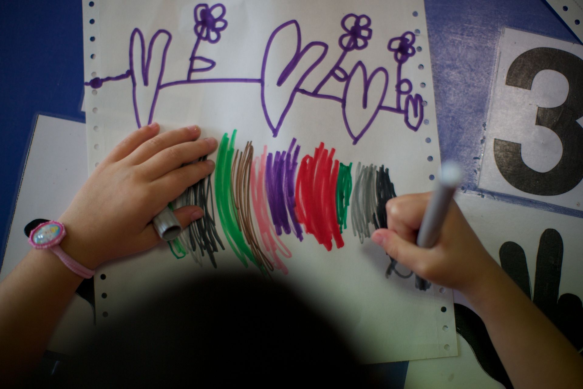 Bambino che colora con vari colori un disegno di fiori e cuori.