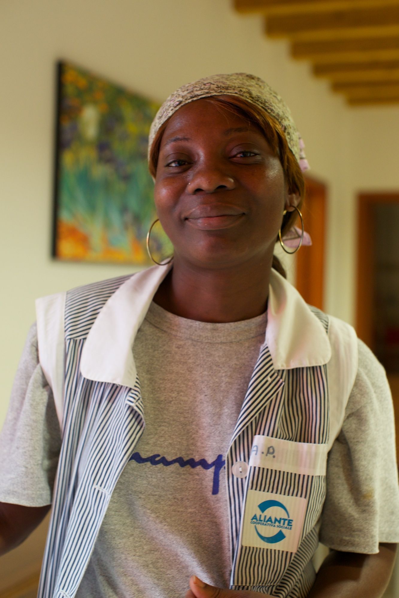Una donna con una camicia grigia e un gilet a righe sorride, in piedi all'interno di un edificio.