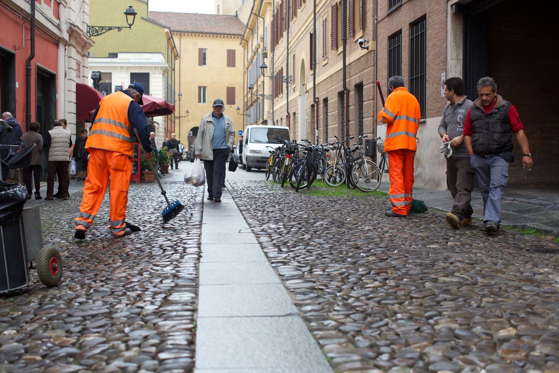 Gli spazzini con i giubbotti arancioni spazzano una strada acciottolata.