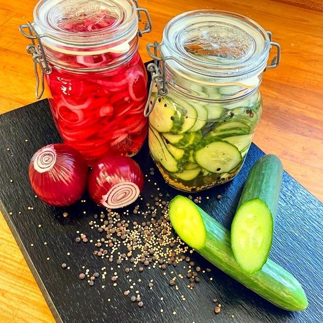 to glas syltede løg og agurker på et skærebræt