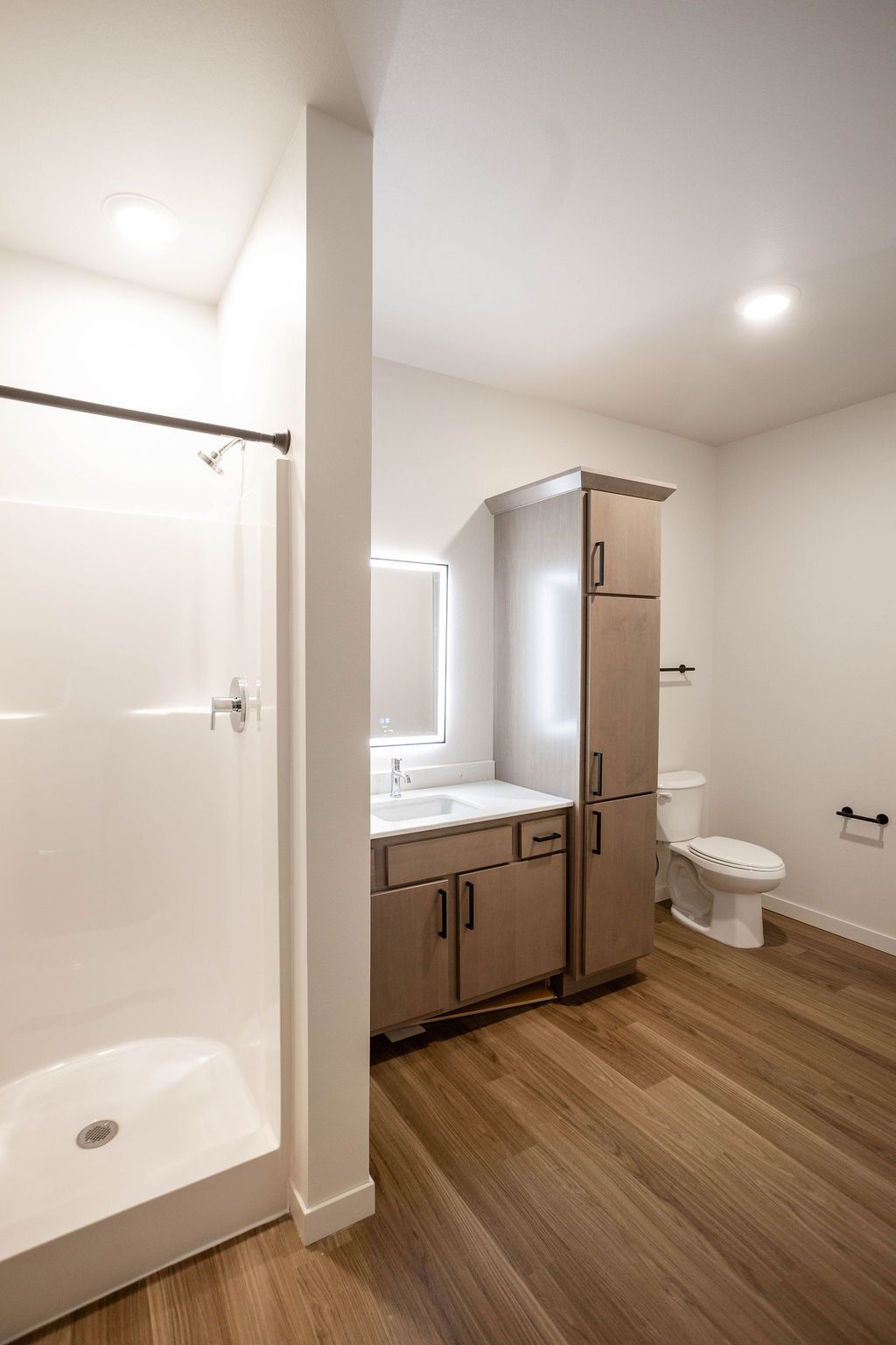 Bathroom with a white shower stall, a vanity with a mirror, and a toilet. The floor is wood-toned.