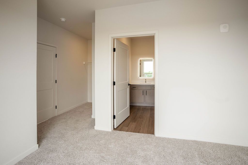 Hallway with carpet leading to an open doorway into a bathroom with a sink and mirror.
