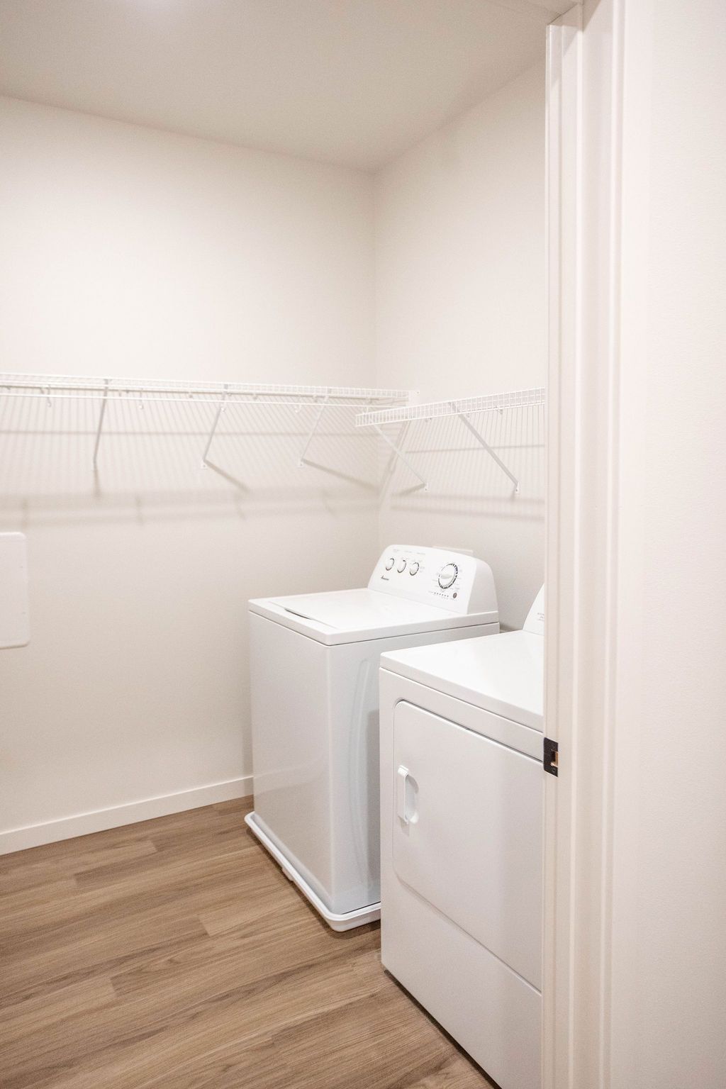 Laundry room with a white washer and dryer, wire shelving, and wood-look flooring.