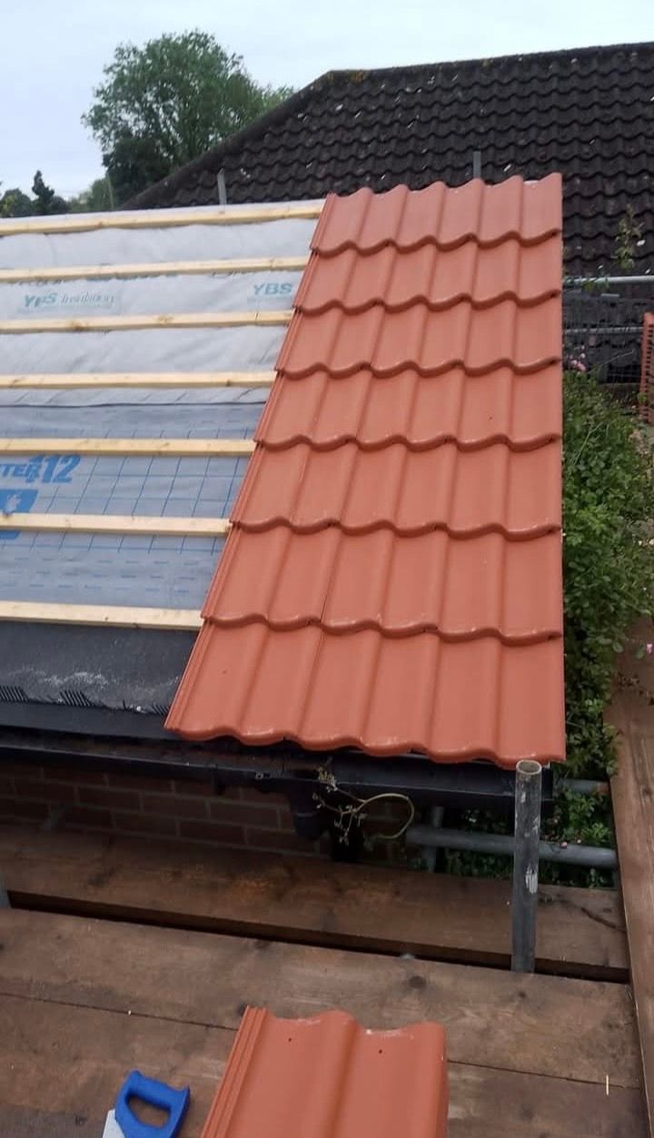 Roof construction with orange tiles being installed on top of wooden rafters and insulation.