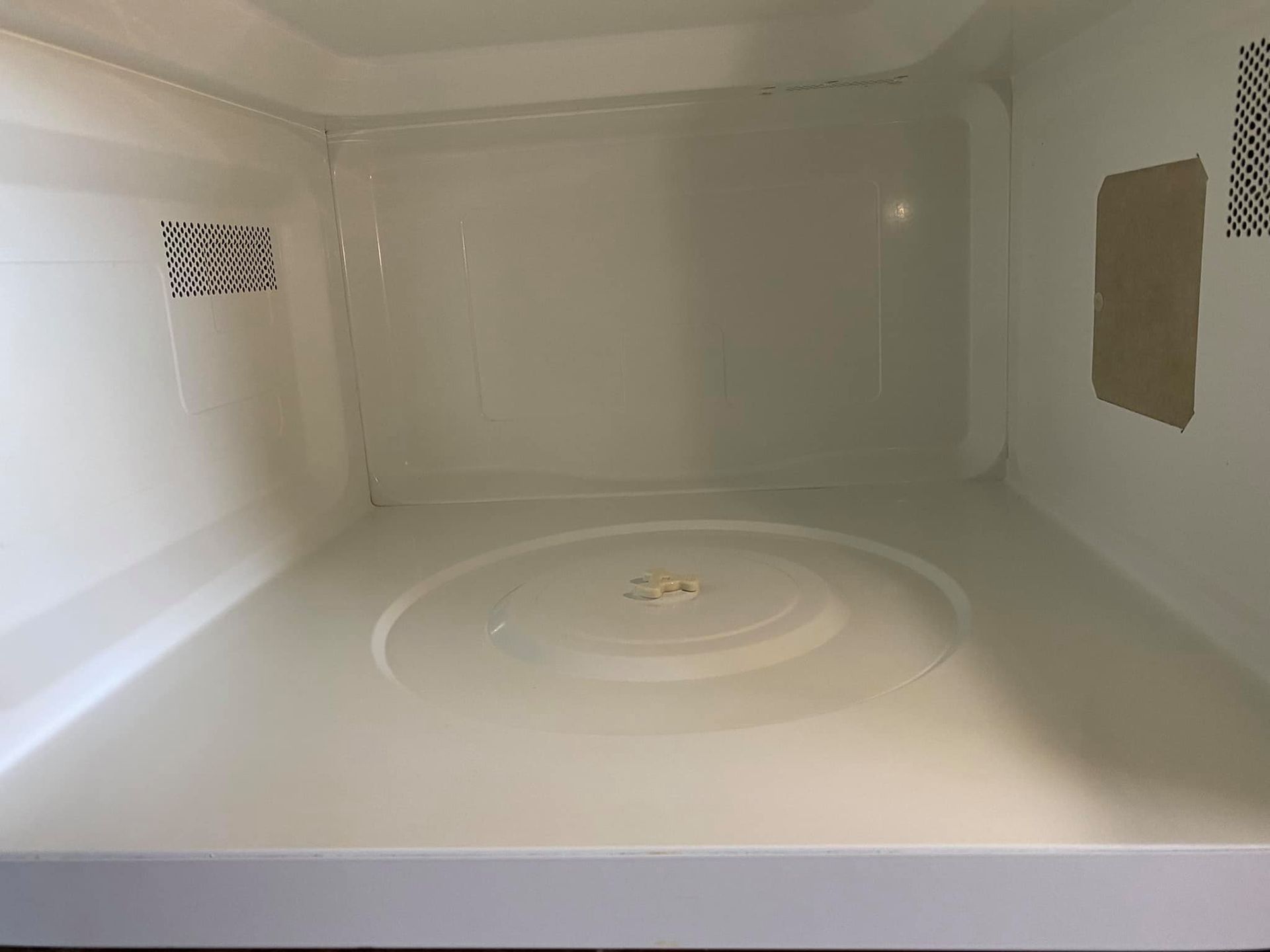 Empty white microwave interior with turntable and side vents