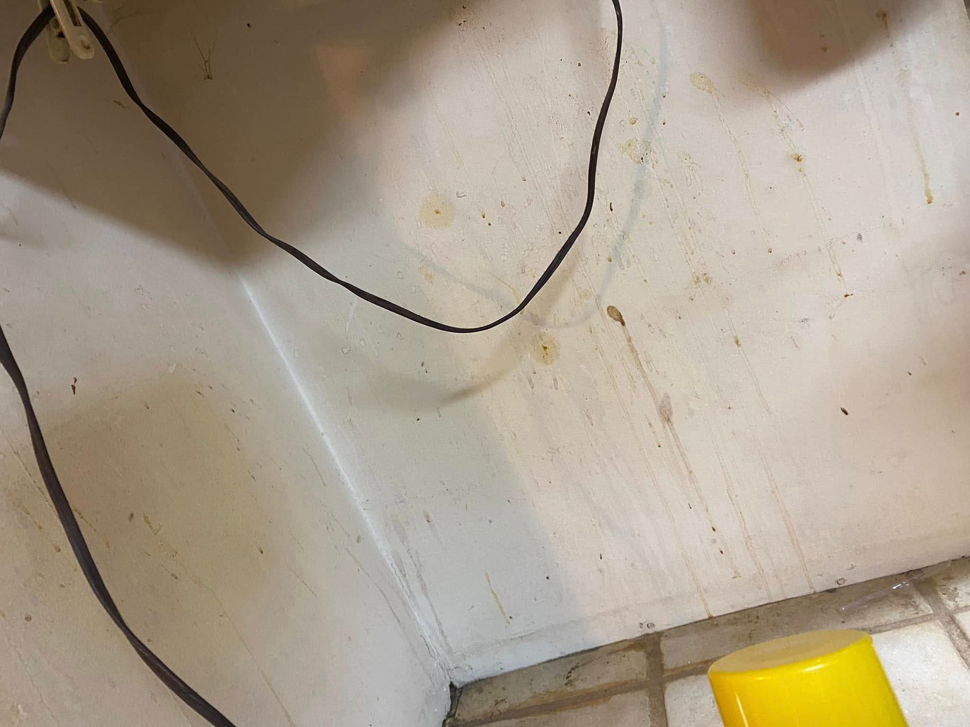 Dirty white wall with black cable and a yellow object at the bottom right.