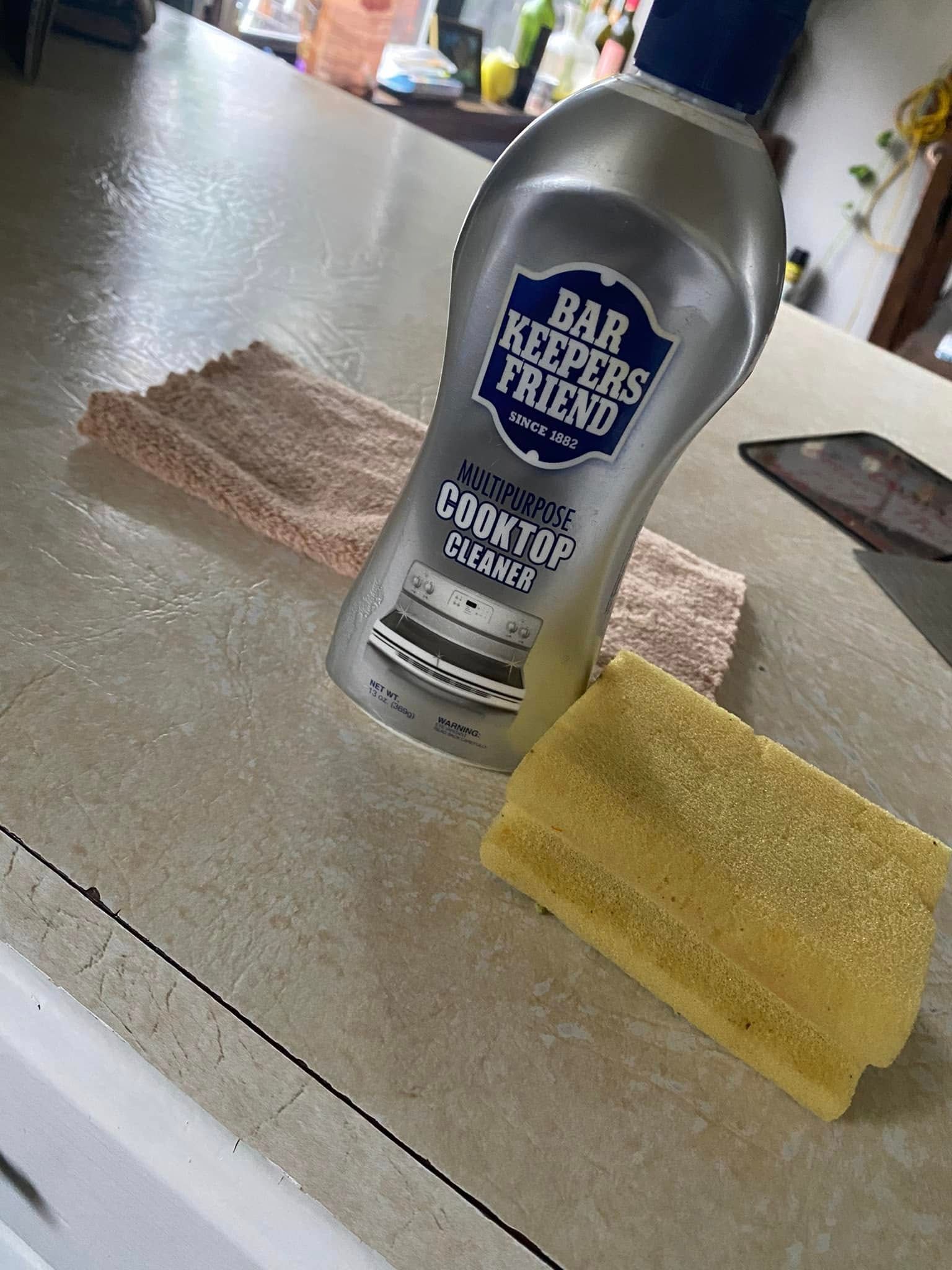 Bottle of Bar Keepers Friend cleanser beside a yellow sponge on a kitchen countertop
