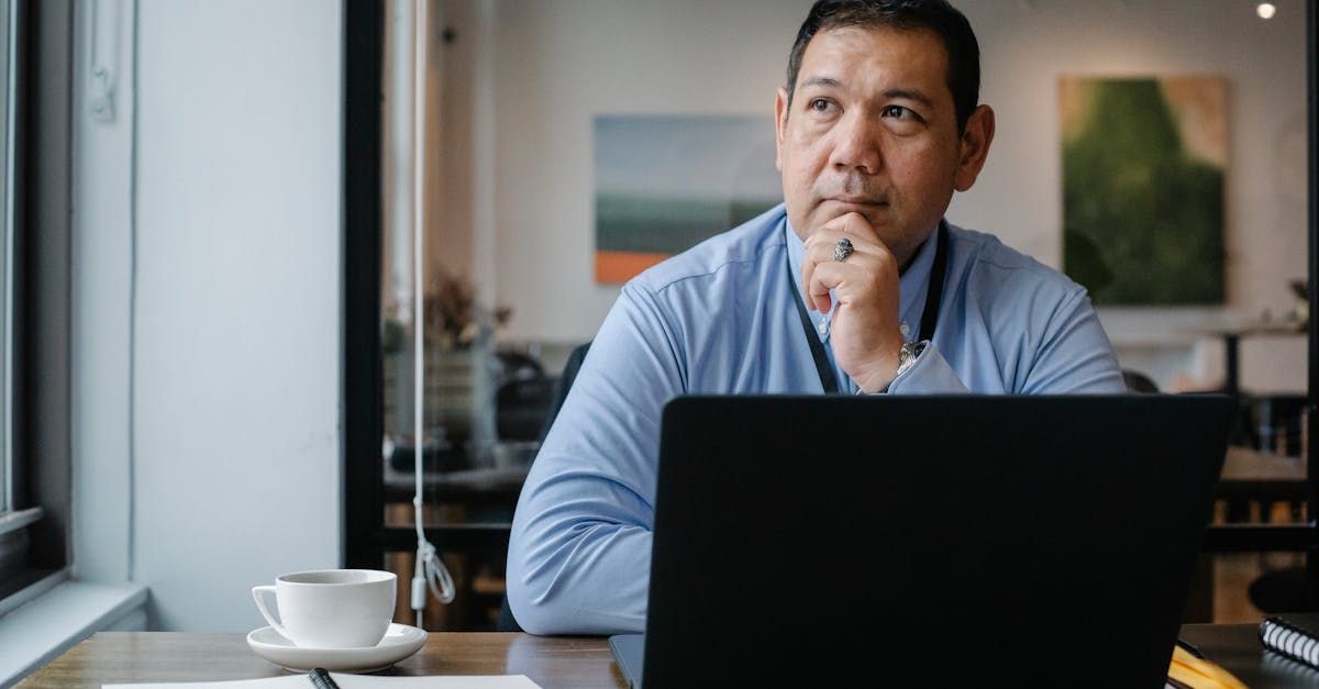 A small business owner is sitting at a table with a laptop and coffee thinking about his website