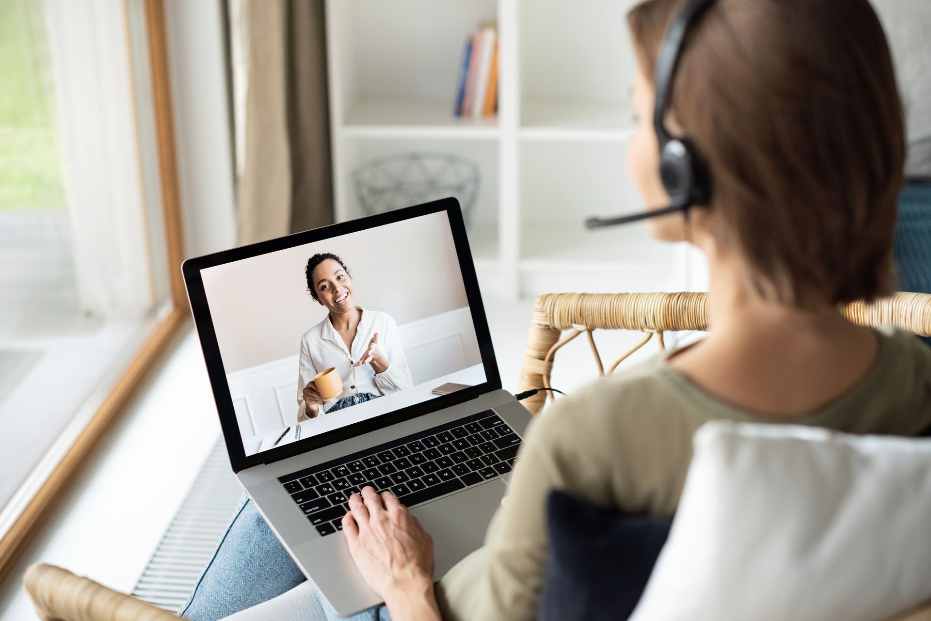 A woman is sitting on a couch using a laptop computer while wearing headphones.