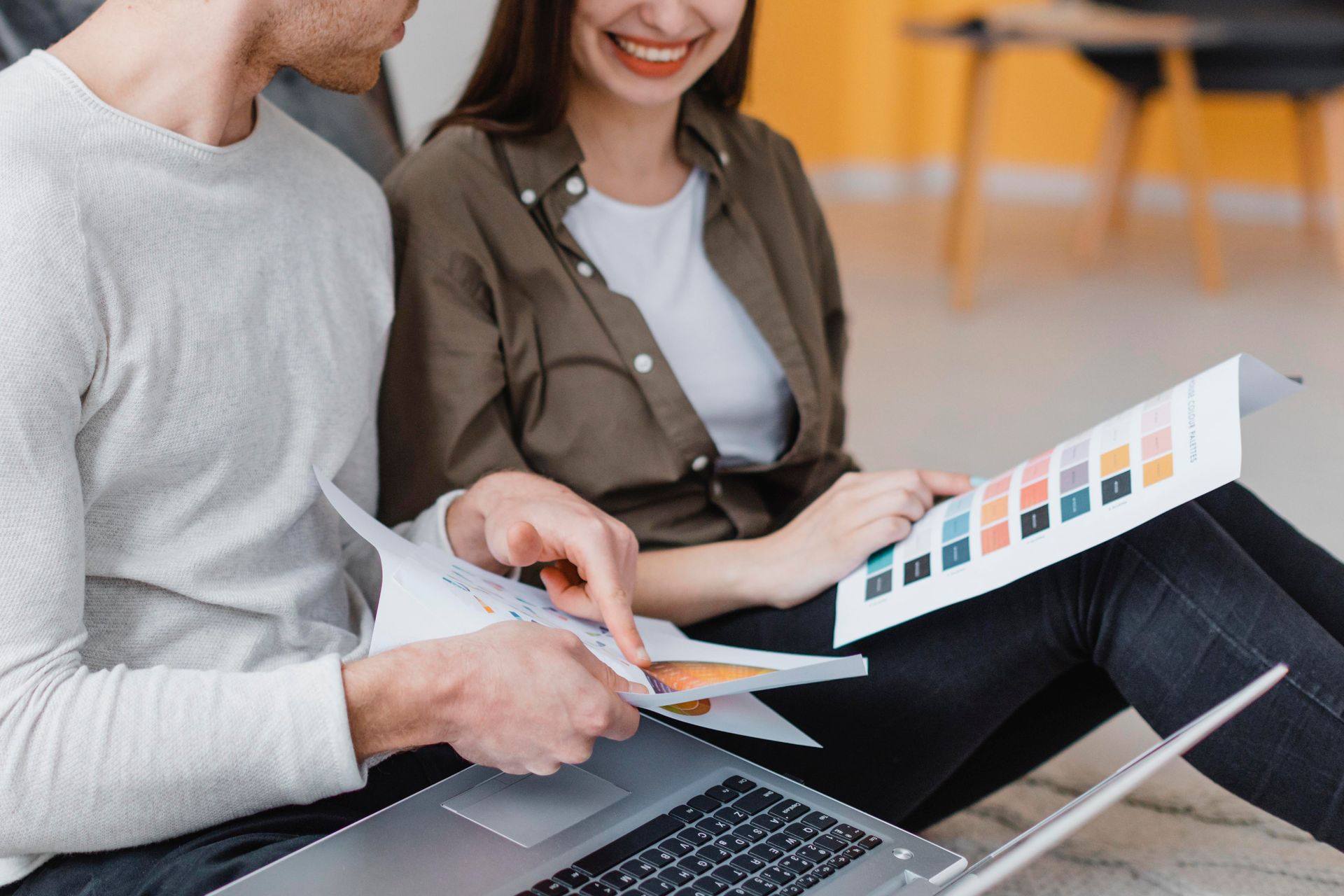 A man and a woman are sitting on the floor with a laptop.