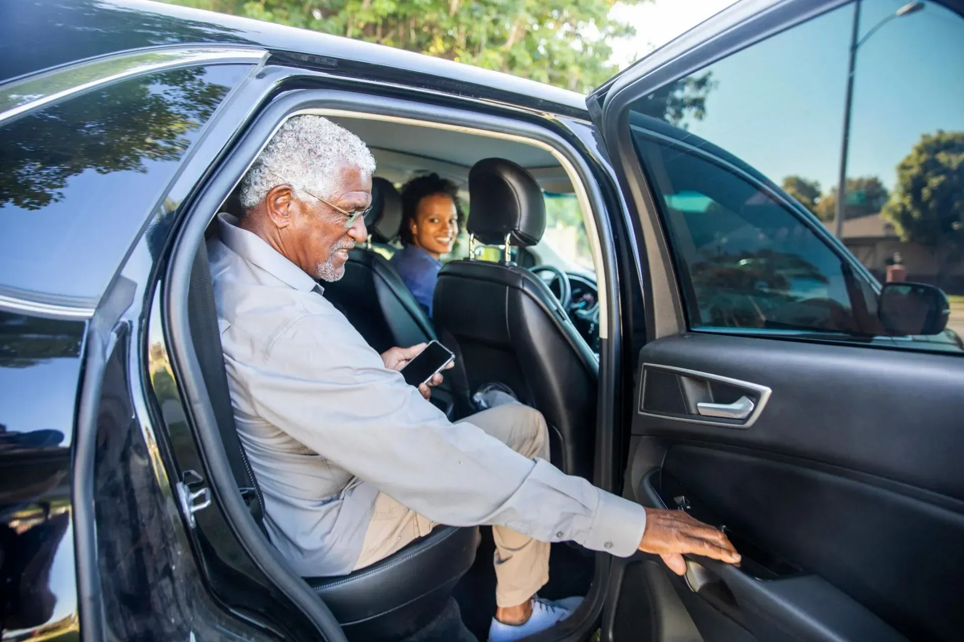 An elderly man is sitting in the back seat of a car.