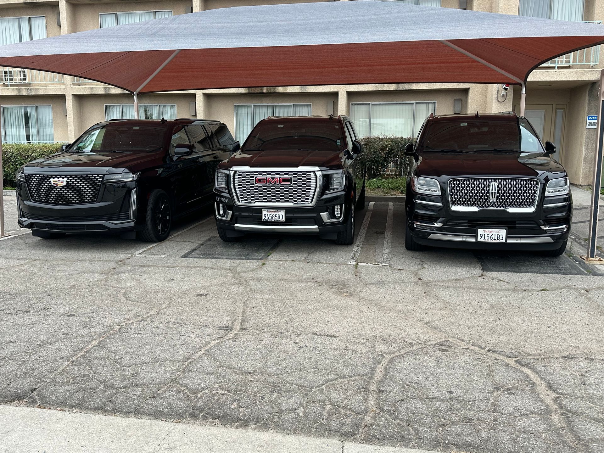 Three black cars are parked under an umbrella in a parking lot.