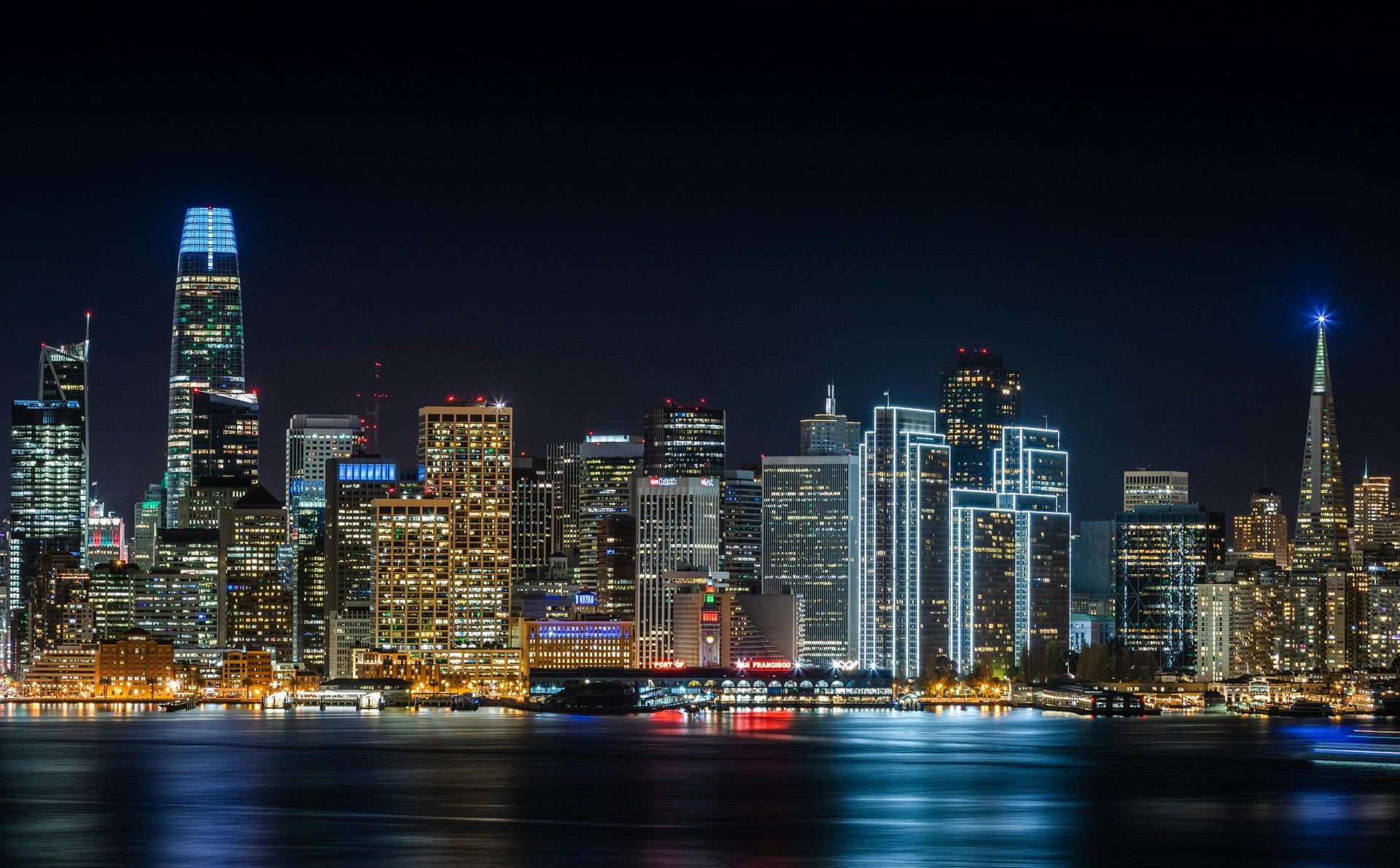 A city skyline at night with a body of water in the foreground