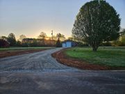 Gravel driveway curves toward a garage and tree at sunrise.