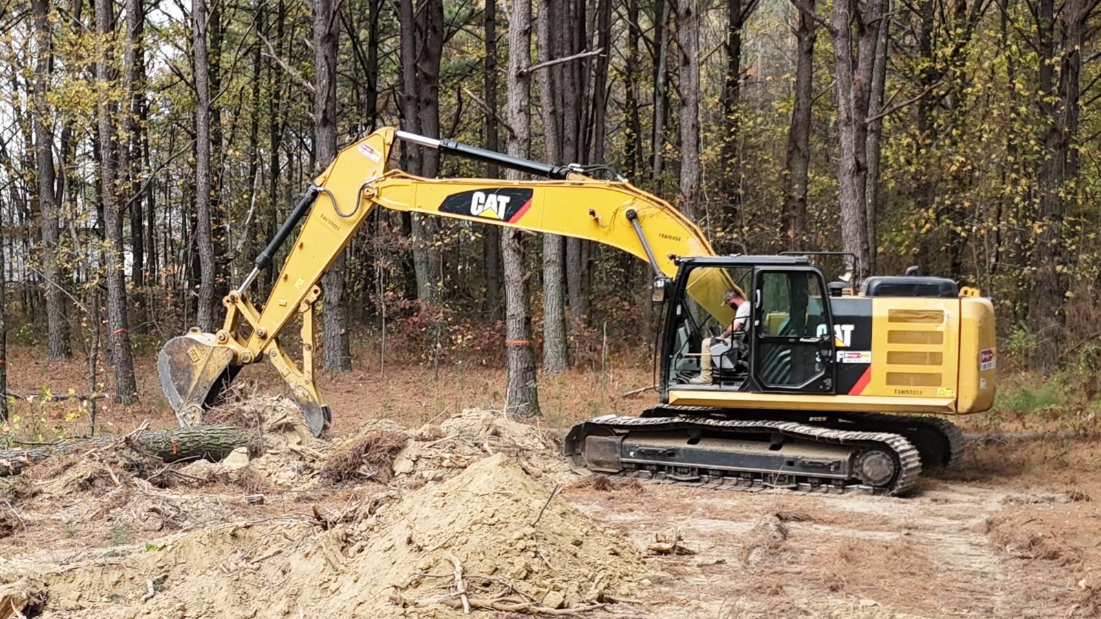 Yellow Caterpillar excavator digging in a wooded area.