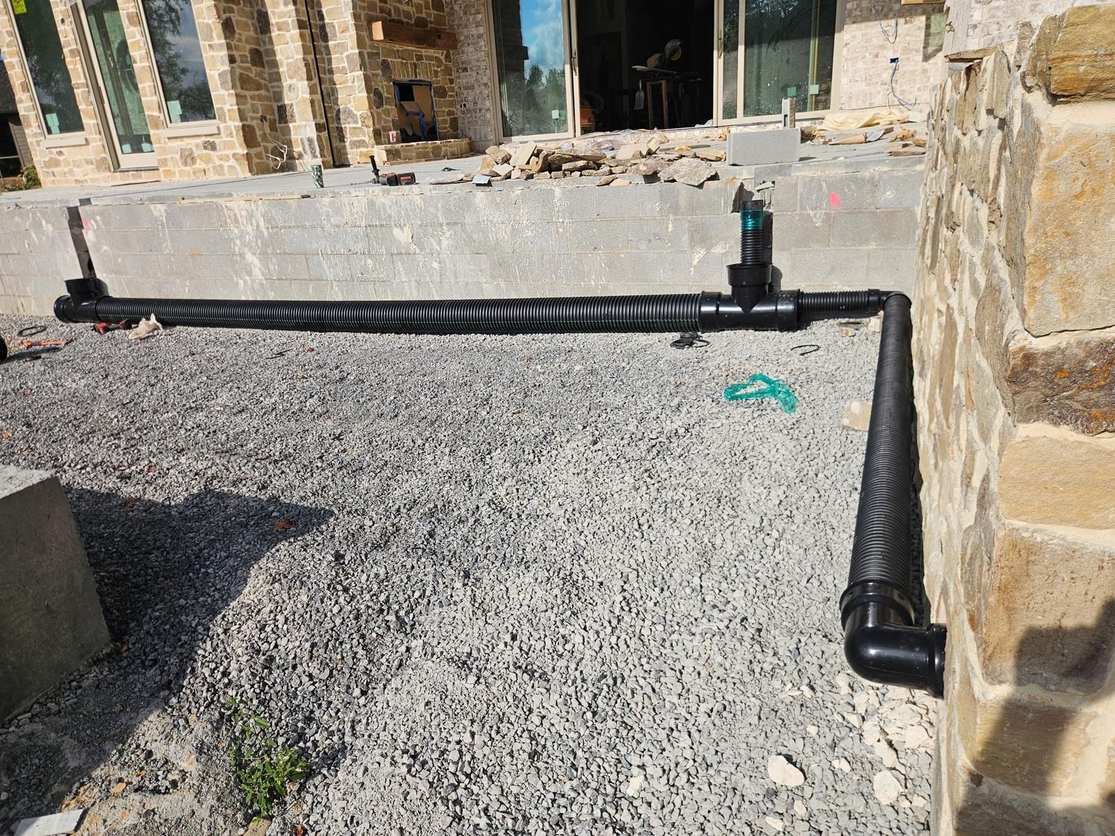 Black pipe irrigation system with valve installed on gravel next to a stone wall.