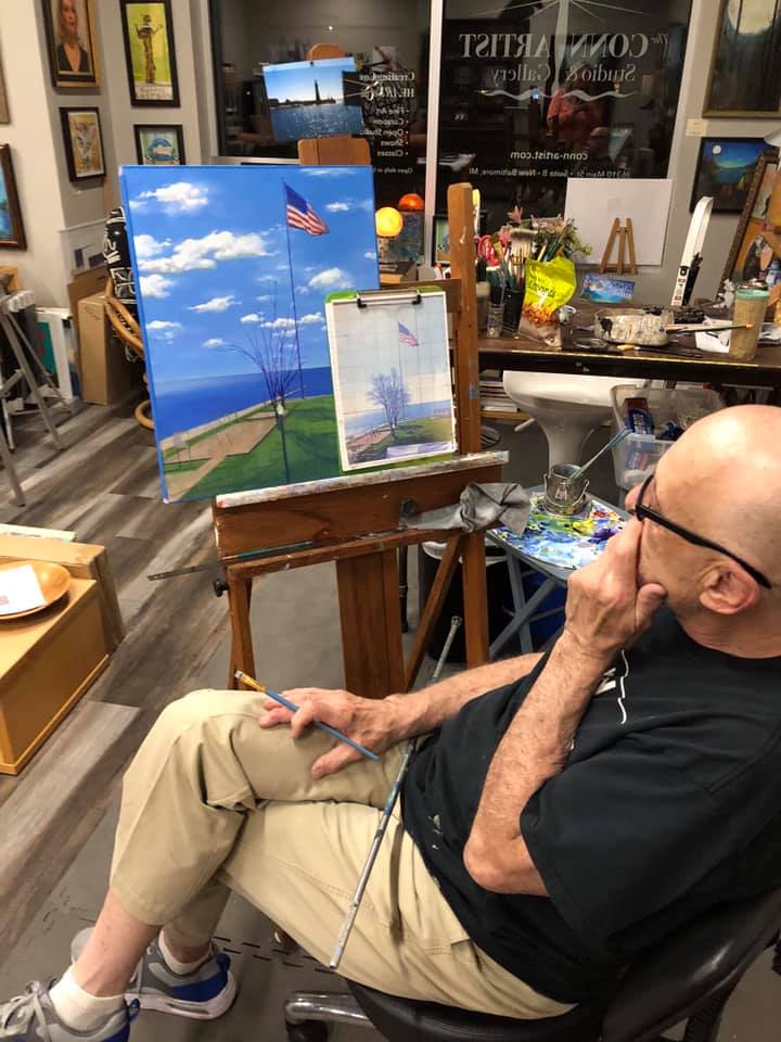 A man is sitting in front of an easel with a painting on it
