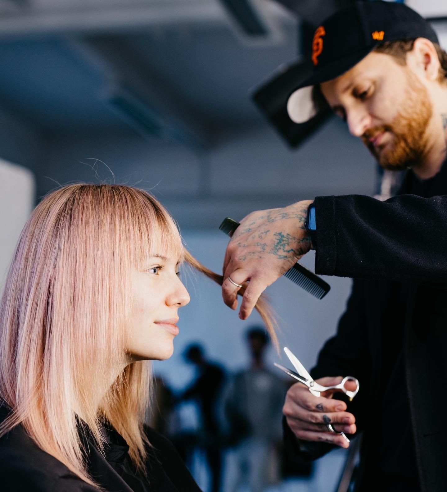 Uomo con capelli acconciati e barba folta, sorridente, che indossa una camicia fantasia, sfondo nero.