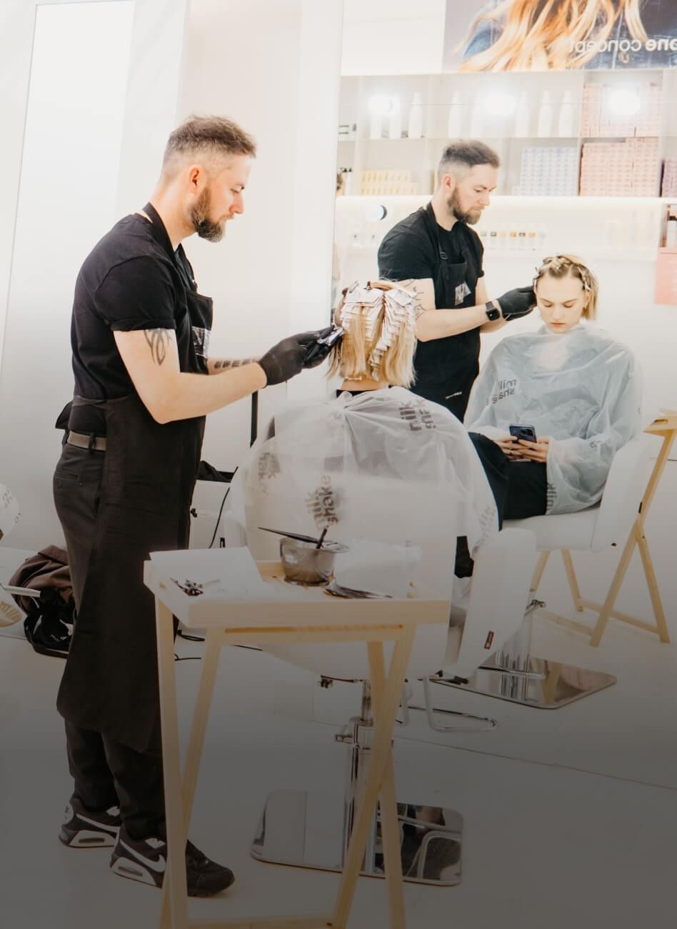 Parrucchiere che usa un ferro arricciacapelli sui lunghi capelli rossi di una cliente in un salone.