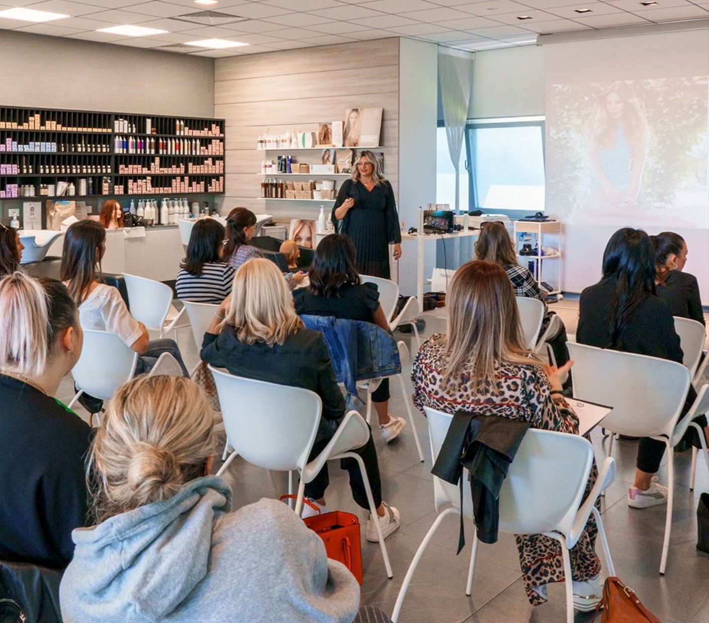 Una mano che regge delle forbici taglia i capelli castani e bagnati sulla testa di un manichino, usando un pettine come guida.