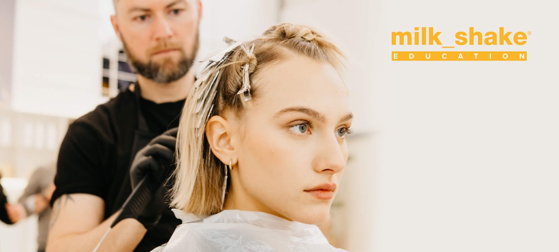 Donna con i capelli castani mossi dal vento, che indossa una camicia bianca su uno sfondo grigio.