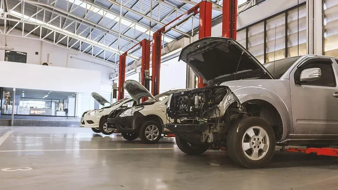 Cars in a repair shop with open hoods; concrete floor, red lifts, and bright lighting. | American Fleet & Auto Service
