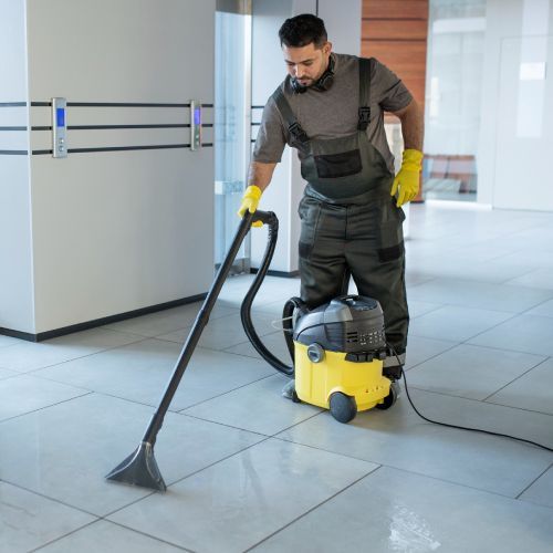 A man is using a yellow vacuum cleaner on a tiled floor.