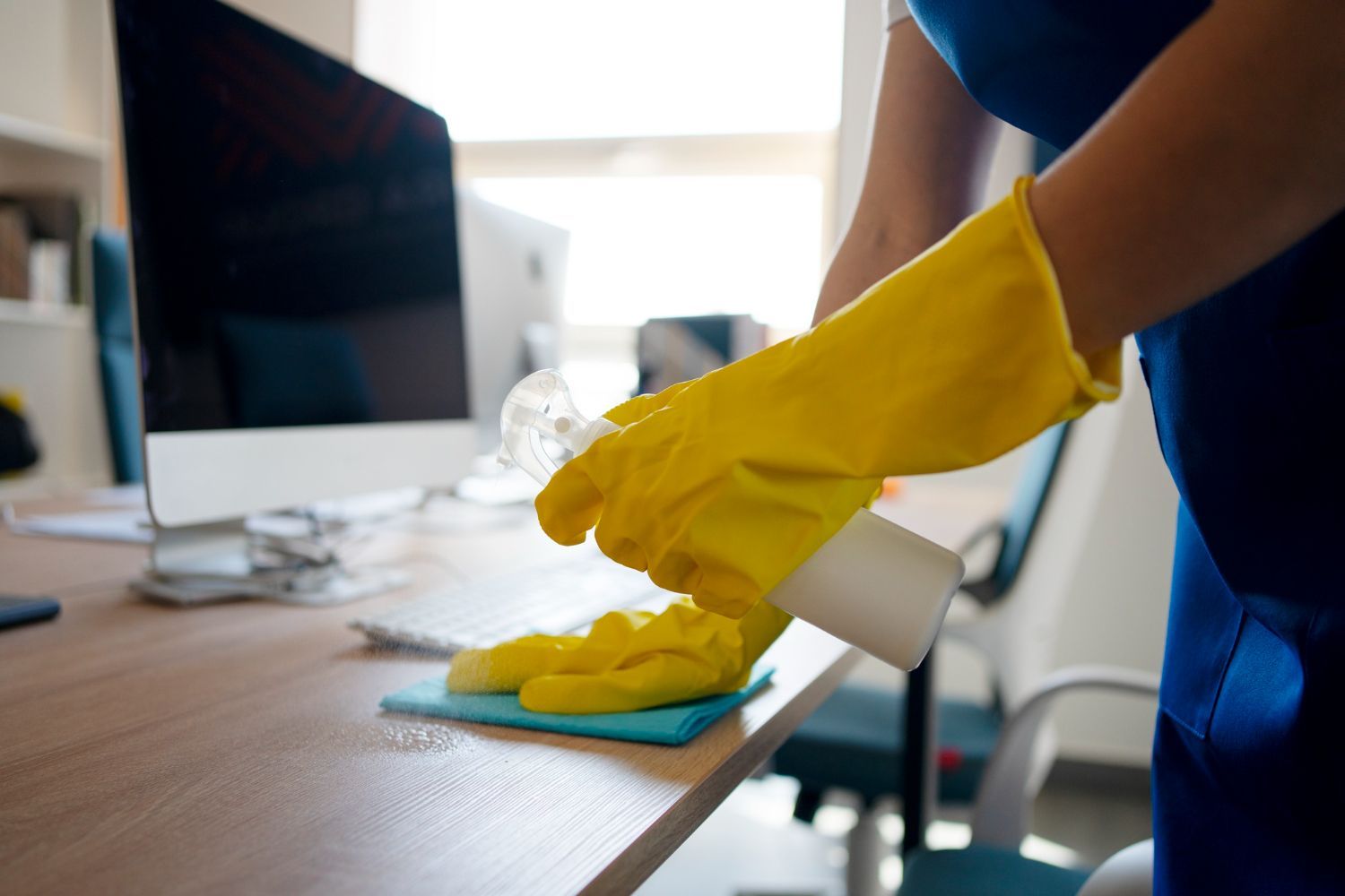 A person wearing yellow gloves is cleaning a desk in an office.