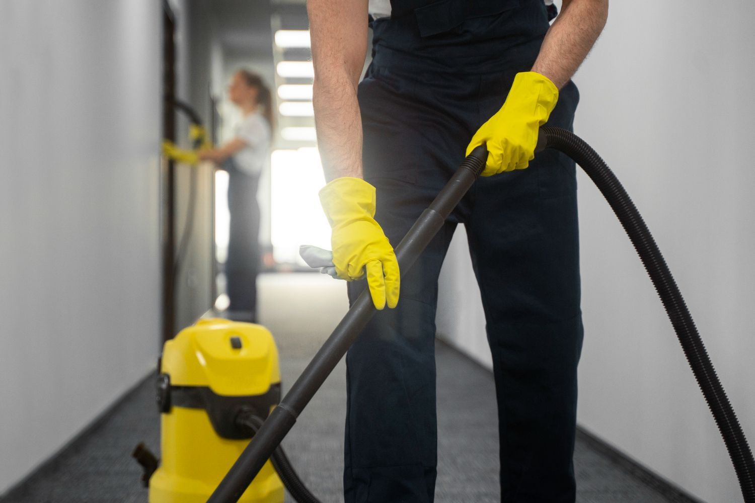 Two people cleaning a hallway with a vacuum cleaner. 