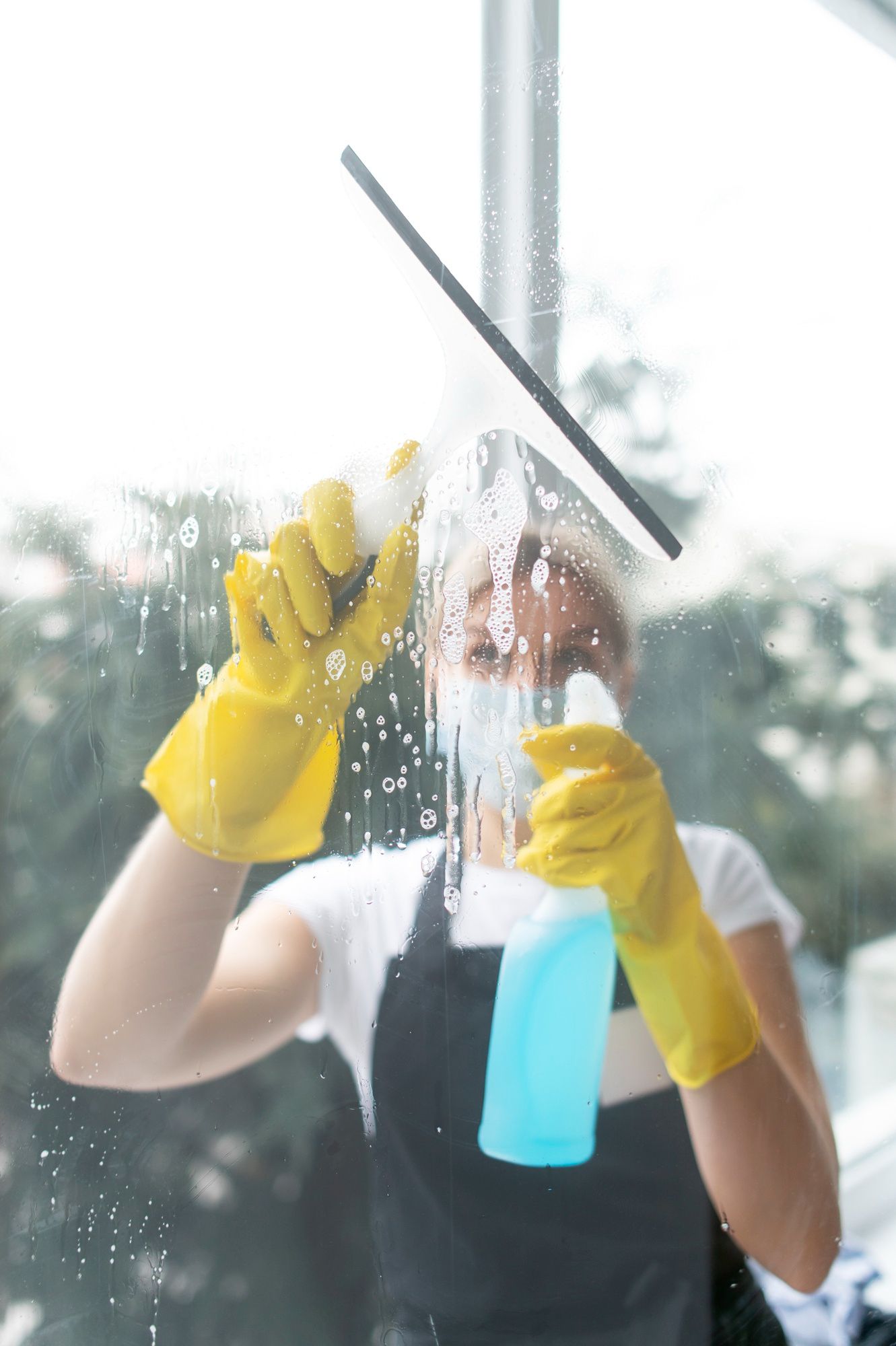 A woman in yellow gloves is cleaning a window with a squeegee.