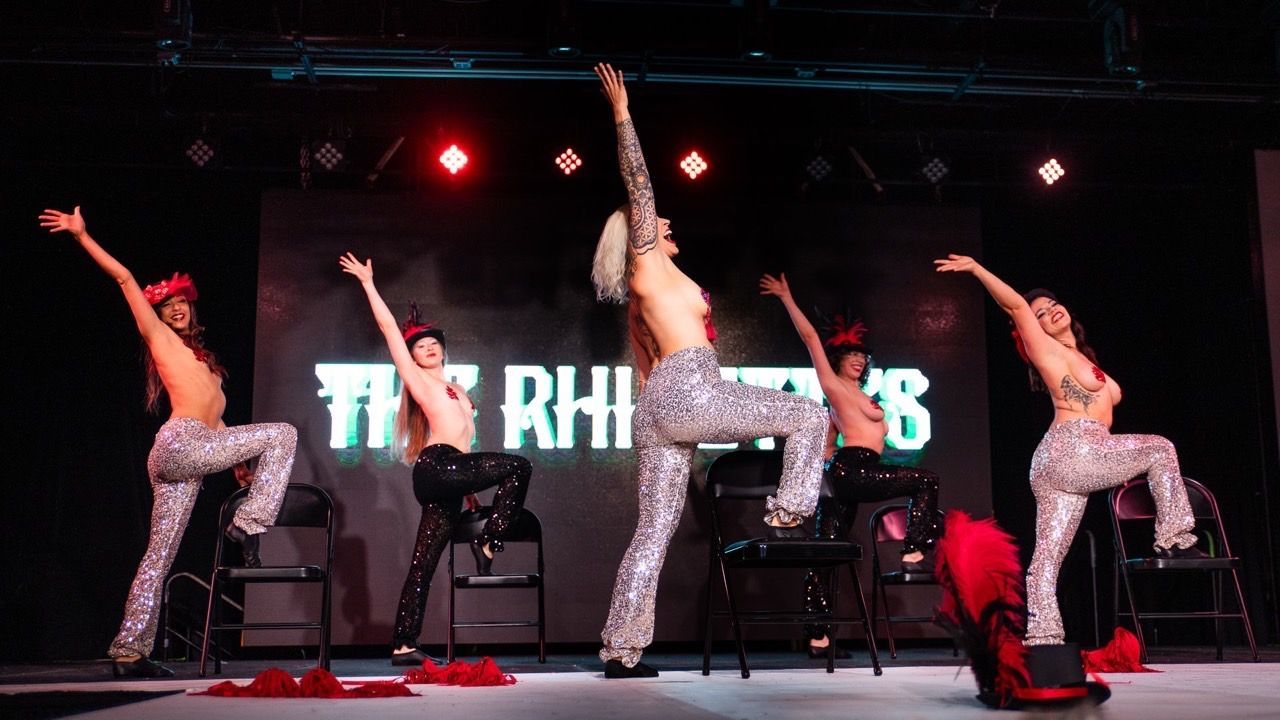 A group of women are dancing on a stage with the word rhinos in the background
