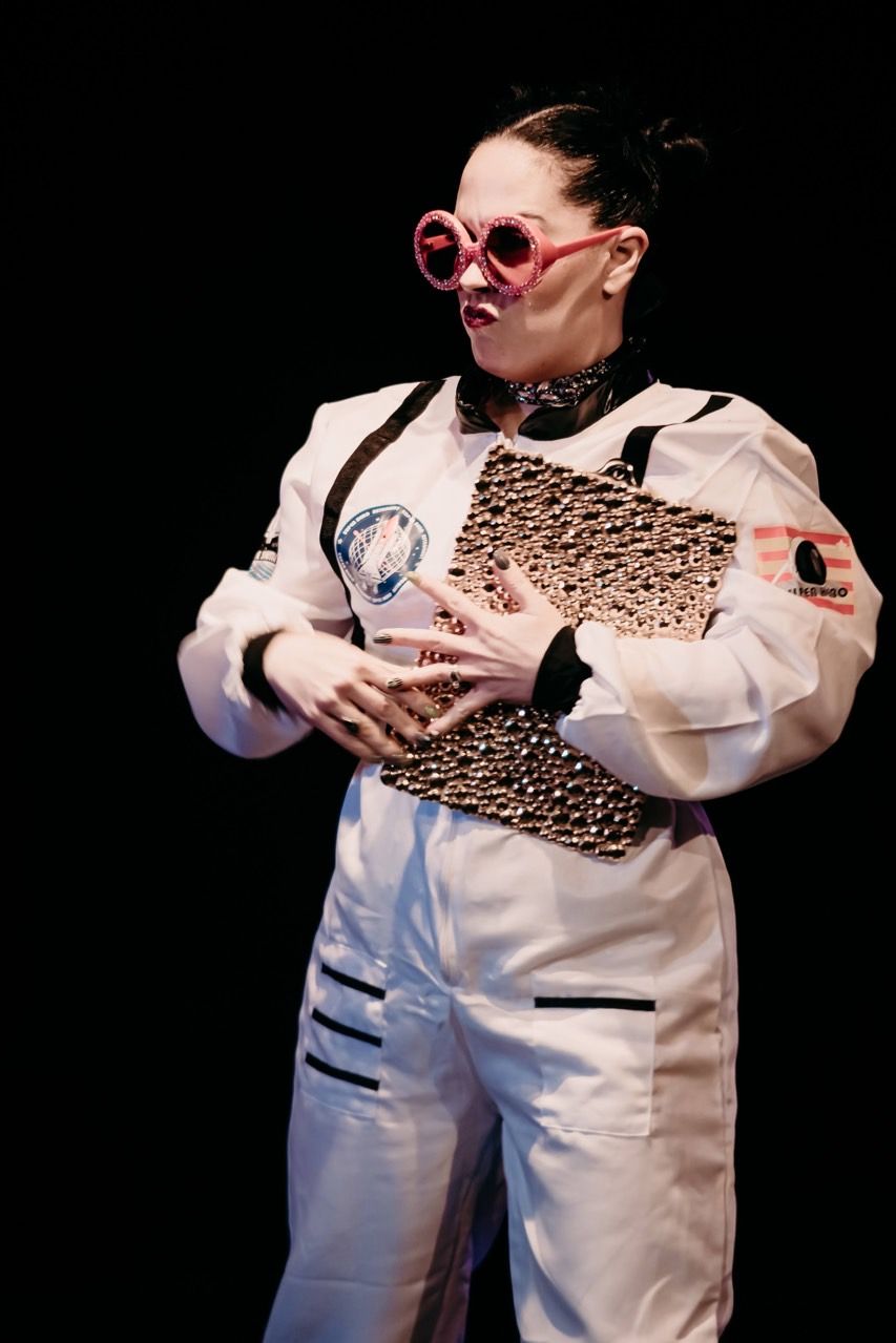 A woman in a white jumpsuit and pink sunglasses is holding a piece of paper.