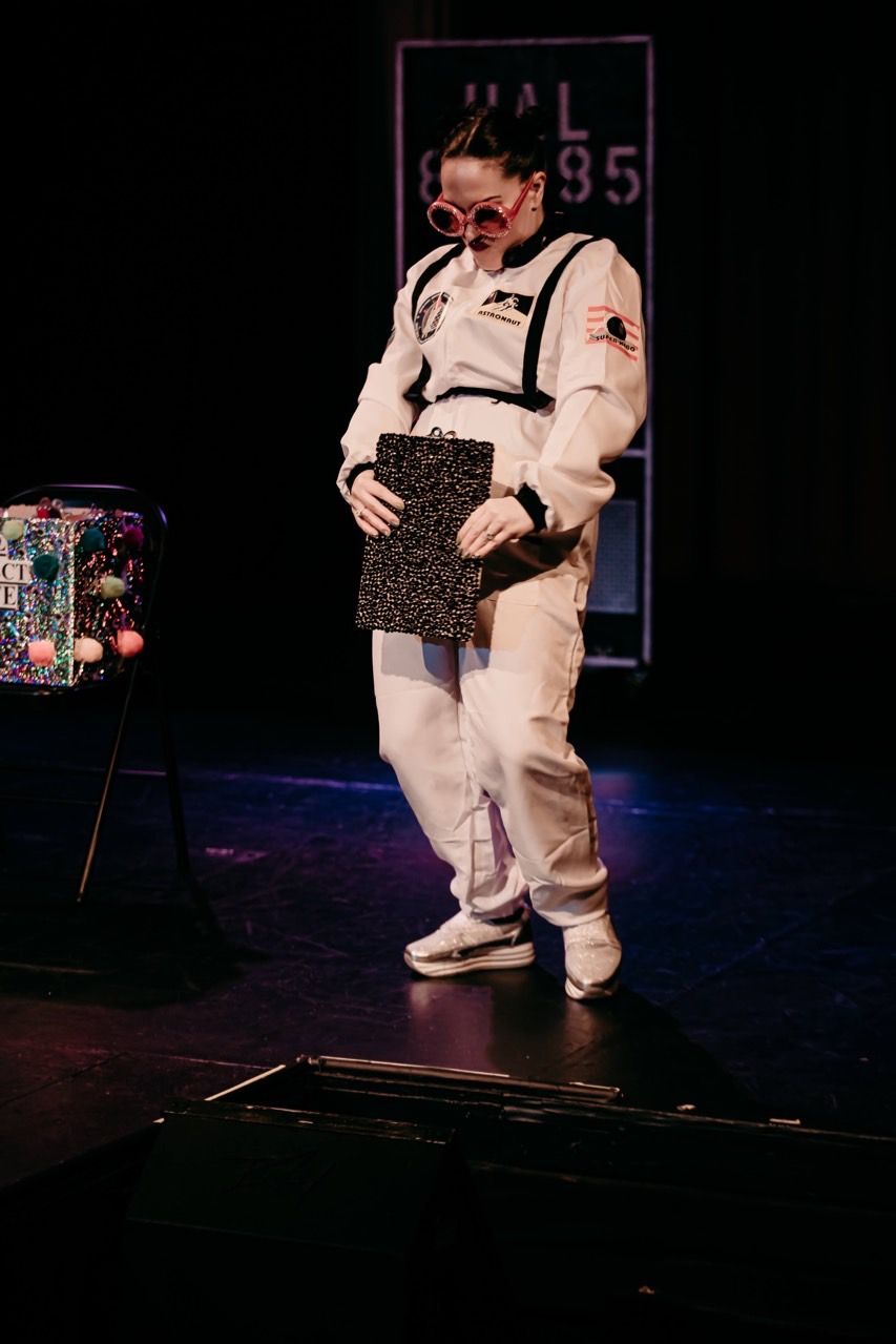 A woman in a space suit is standing on a stage holding a box.