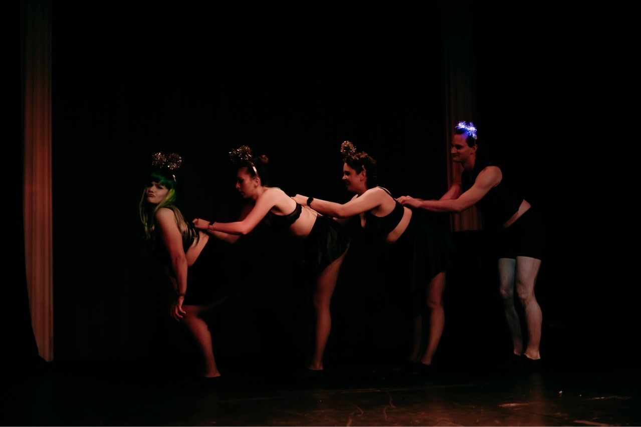 A group of women are dancing on a stage in a dark room.