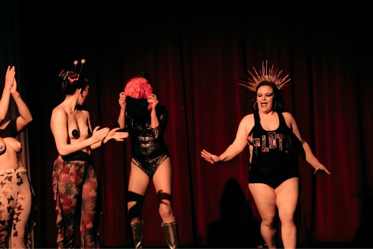 A group of women are dancing on a stage in front of a red curtain.