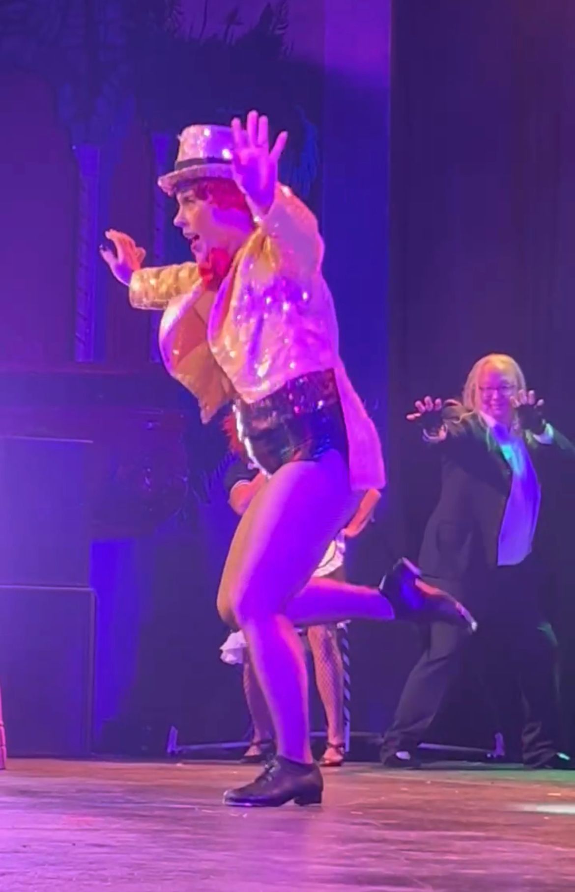 A group of people are dancing on a stage with purple lights.